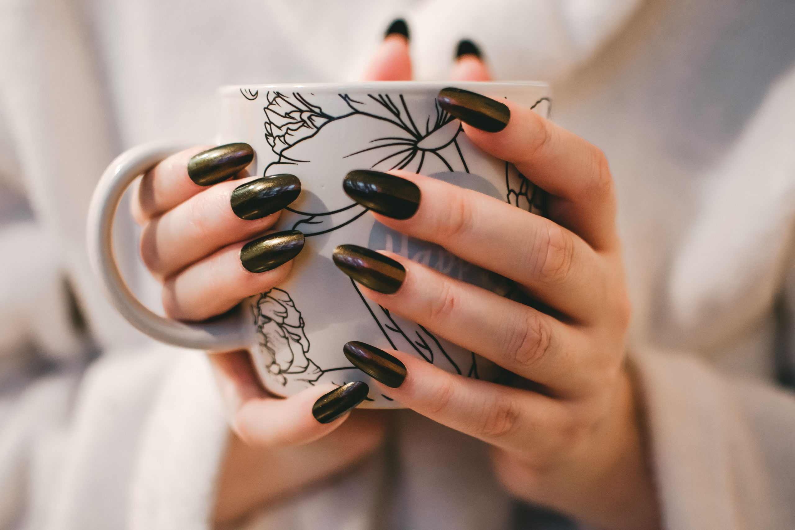 Black and gold manicure holding a warm mug